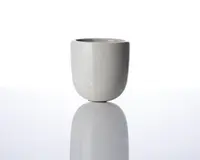 En lille, rund, lysegrå keramikkop med en glat mat overflade. Koppen har lige sider og en let afrundet bund, uden synligt håndtag eller dekoration. Det minimalistiske design giver den et moderne og elegant udtryk.