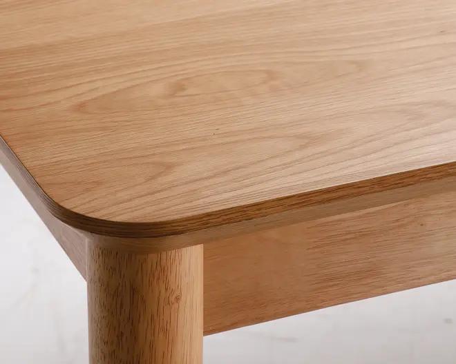 Nærbillede af en træoverflade med en glat, afrundet hjørne og synlig træstruktur. Overfladen har en lys og naturlig finish, der fremhæver træets mønster og tekstur. Benet er cylindrisk og sidder solidt fast på toppen, hvilket giver et robust og moderne udtryk.