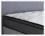 Nærbillede af et madras-hjørne med en tyk, blød, quiltet top i hvidt stof med diskrete sorte swirl-mønstre. Siderne er betrukket med mørkegråt stof med kvadratsyninger, og madrassen har forstærkede kanter for ekstra holdbarhed.