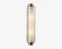 En lodret vægmonteret lampe med cylindrisk form og klare, riflede glaspaneler. Enderne er afsluttet med metalbeslag i messingfarve, hvilket giver lampen et vintage-inspireret udtryk. Lyset indeni udsender en varm, diffus glød gennem det strukturerede glas, hvilket skaber et elegant og sofistikeret udseende.