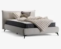 Moderne polstret sengegavl i lysebeige stof med høj, blød hovedgavl. Sengen har en tyk, mørkegrå madras og hvid topmadras. Sengetøjet består af en creme- og taupe-stribet dyne, matchende pudebetræk samt dekorative pyntepuder i neutrale farver og en rund, plisseret pude. Sengen står på slanke, skråtstillede sorte ben.