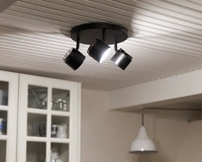 Loftmonteret lampearmatur med tre justerbare spotlys i mat sort finish. Hvert spotlys kan rettes individuelt, hvilket giver mulighed for tilpassede lysvinkler. Armaturet har en rund base, der sidder tæt mod loftet, og spotlysene har et moderne, cylindrisk design med metalliske detaljer for enderne.