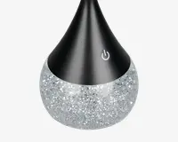 Produktet har et dråbeformet design med en mat sort øverste del og en glitrende, sølvfarvet nederste del. Der er et touchfølsomt tænd/sluk-ikon på den sorte overflade, hvilket indikerer nem betjening. Den glitrende bund giver et dekorativt og stilfuldt udseende, som passer godt til moderne indretning.
