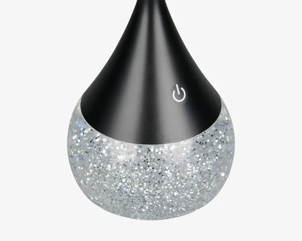 Produktet har et dråbeformet design med en mat sort øverste del og en glitrende, sølvfarvet nederste del. Der er et touchfølsomt tænd/sluk-ikon på den sorte overflade, hvilket indikerer nem betjening. Den glitrende bund giver et dekorativt og stilfuldt udseende, som passer godt til moderne indretning.