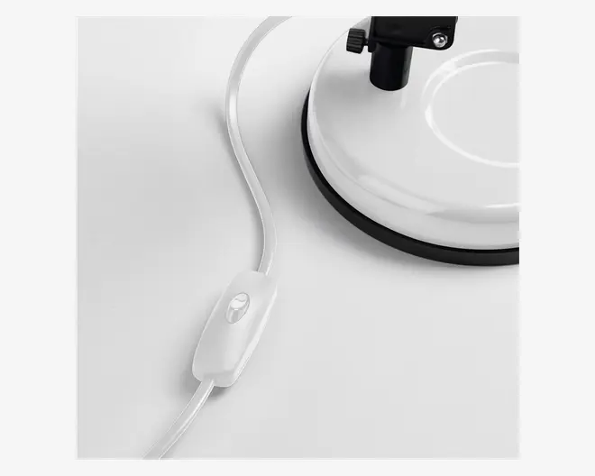 Nærbillede af en hvid, rund base med sort kant, der har en strømledning med en indbygget tænd/sluk-knap. Kontakten er oval og har samme farve som ledningen, hvilket gør den nem at betjene.