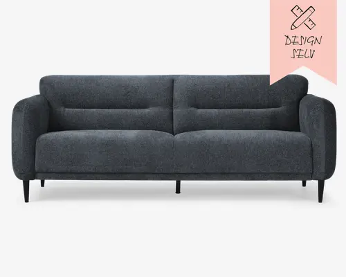 Moderne mørkegrå sofa med blødt, tekstureret stofbetræk. Sofaen har dybe, polstrede sæde- og ryghynder med diskrete horisontale syninger for ekstra komfort og stil. Den har afrundede armlæn og slanke, koniske sorte ben, hvilket giver et elegant og tidløst udtryk. Designet er enkelt og minimalistisk, hvilket passer til mange forskellige indretninger.