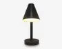 En moderne bordlampe med mat sort finish, der har en konisk lampeskærm, som leder lyset nedad. Lampen har en cylindrisk fod og en lige, slank stang, hvilket giver et minimalistisk og nutidigt udtryk. Lyset er varmt og diffust, hvilket egner sig til at skabe en hyggelig stemning.