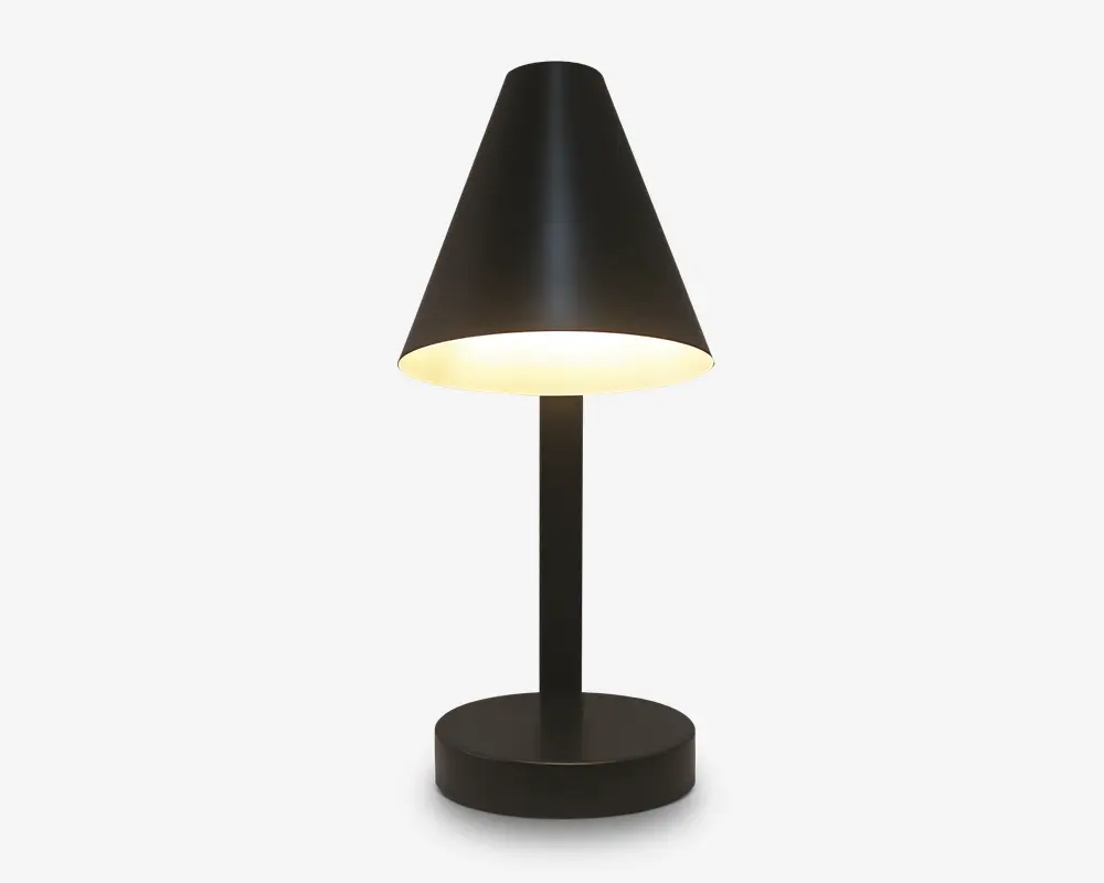 En moderne bordlampe med mat sort finish, der har en konisk lampeskærm, som leder lyset nedad. Lampen har en cylindrisk fod og en lige, slank stang, hvilket giver et minimalistisk og nutidigt udtryk. Lyset er varmt og diffust, hvilket egner sig til at skabe en hyggelig stemning.