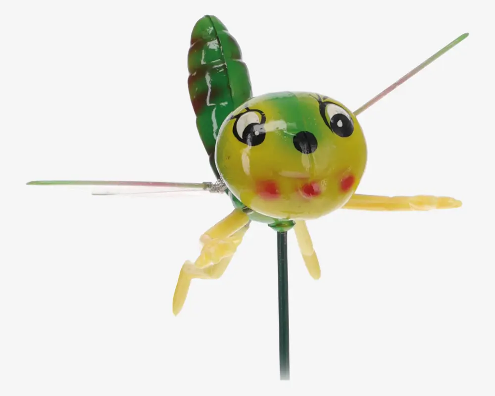 En dekorativ havefigur formet som et fantasifuldt insekt med en rund gul og grøn krop, store tegneserieagtige øjne, røde kinder og en lille sort næse. Den har to gule ben, to tynde metalvinger og en grøn bladlignende hale. Figuren er monteret på en tynd metalpind, så den nemt kan placeres i jorden.