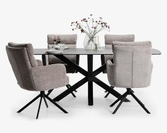 Et moderne spisesæt med et rektangulært bord, der har en mat sort metalbase og en glat, mørk bordplade. Sættet inkluderer seks polstrede stole i lysegråt stof, hver med høj ryg, armlæn og sorte metalben med drejefunktion. Bordet er pyntet med en klar glasvase med fine blomster, og der er dækket op med tallerkener, glas og bestik samt to vinglas med rødvin.