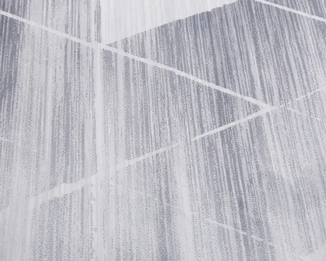 Nærbillede af et stof med et moderne geometrisk mønster. Designet har diagonale linjer og overlappende former i grå og hvide nuancer, hvilket skaber en tekstureret, lagdelt effekt. Linjerne varierer i tykkelse og tæthed, hvilket giver stoffet et dynamisk, nutidigt udseende.
