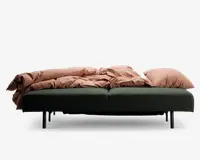 Et moderne, lavt møbel med en dybgrøn polstret bund og sorte cylindriske ben. Overfladen er dækket af blødt, rustfarvet sengetøj og to store matchende puder, hvilket giver et hyggeligt og indbydende udtryk. Det samlede design er minimalistisk og nutidigt, velegnet til både at sidde og slappe af på.