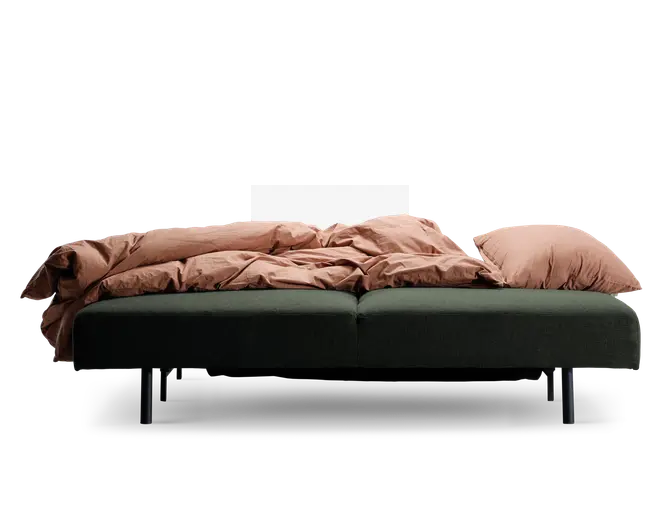 Et moderne, lavt møbel med en dybgrøn polstret bund og sorte cylindriske ben. Overfladen er dækket af blødt, rustfarvet sengetøj og to store matchende puder, hvilket giver et hyggeligt og indbydende udtryk. Det samlede design er minimalistisk og nutidigt, velegnet til både at sidde og slappe af på.