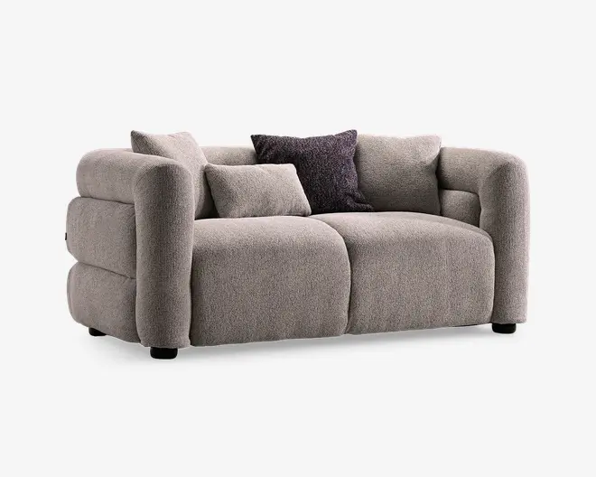 En lysegrå sofa med lav profil, afrundede armlæn og bløde hynder, vist med tre pyntepuder, herunder en mørk tekstureret pude.