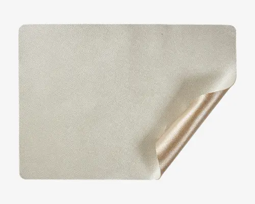 Et rektangulært stykke materiale med en glat, mat lysebeige overflade og afrundede hjørner. Det ene hjørne er let løftet og afslører en blank, metallisk gylden bagside. Kanterne er pænt afsluttede, og materialet virker fleksibelt og tyndt.