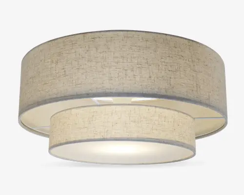 Et moderne loftarmatur med dobbelt tromledesign bestående af to koncentriske stofskærme i en neutral beige farve. Den ydre skærm er større og omgiver en mindre indre skærm, begge med et diskret tekstureret mønster. Bunden er dækket af en mat diffuser, der giver et blødt og jævnt lys. Armaturet har et rent, moderne udtryk, der passer til mange forskellige indretninger.