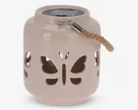 En rund, lysebeige lanterne af keramik med udskårne sommerfugle på siderne. Den har et kraftigt rebhåndtag, der er fastgjort med en metalbeslag, og et solpanel på toppen til opladning. Lanternen har en glat, blank overflade og er velegnet til udendørs eller dekorativ brug.