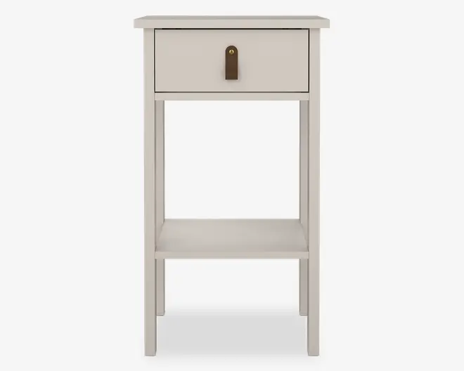 Et kompakt, rektangulært bord med en glat, lysebeige finish. Bordet har en enkelt skuffe øverst med en brun læderstrop og en guldfarvet nitte som greb. Under skuffen er der en åben hylde til ekstra opbevaring. Bordet står på fire lige ben, hvilket giver det et enkelt og moderne udtryk.