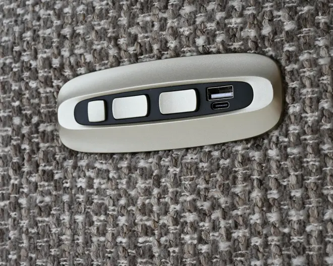 Lille oval beige styreenhed med sort midterpanel, tre hvide rektangulære knapper og en lille port eller indikator til højre, vist på en grå struktureret stofbaggrund.