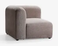 Dette møbel har et moderne, minimalistisk design med armlæn på højre side. Det er polstret med et blødt, tekstureret lysebrunt stof. Sædet og ryglænet er tykt polstrede for ekstra komfort, og armlænet er bredt og afrundet, hvilket matcher det bløde og indbydende udtryk. Basen er lav, hvilket giver et solidt og stabilt udseende.