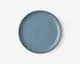 Rund tallerken med en glat, blank overflade i en afdæmpet blå farve. Kanten er tynd og let hævet med en diskret mørkere kant. Overfladen er jævn og uden tekstur, hvilket giver et moderne og minimalistisk udtryk.