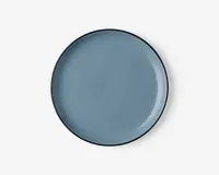 Rund tallerken med en glat, blank overflade i en afdæmpet blå farve. Kanten er tynd og let hævet med en diskret mørkere kant. Overfladen er jævn og uden tekstur, hvilket giver et moderne og minimalistisk udtryk.