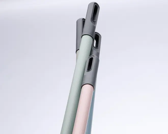 Nærbillede af tre skaft til rengøringsredskaber i pastelfarver (mintgrøn, lyserød og lyseblå). Hvert skaft har et tekstureret greb og en grå plastiktop med et ovalt ophængningshul for nem opbevaring.