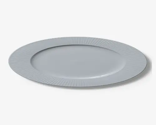 Rund hvid tallerken med bred kant, der har en diskret, jævnt fordelt rillet struktur. Midten af tallerkenen er glat og enkel, hvilket giver et rent og elegant udtryk, der passer til både hverdag og festlige lejligheder.