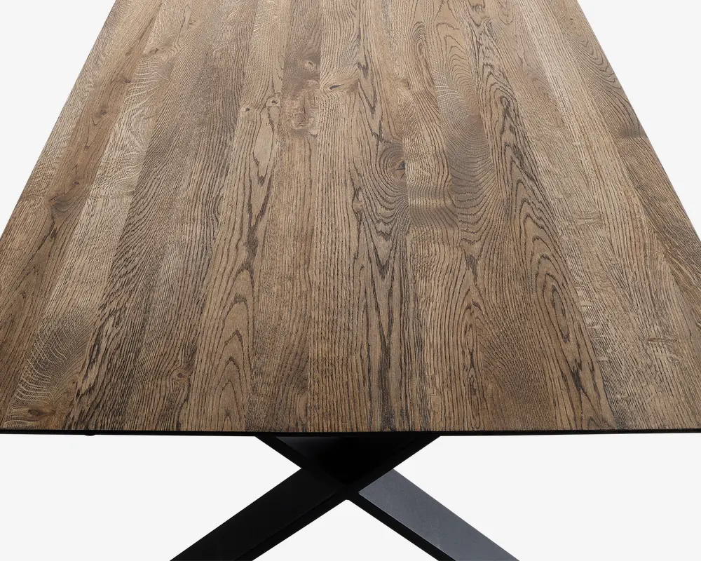 Rektangulær bordplade lavet af naturtræ med synligt åremønster og en glat, mat overflade. Træet har en varm, mellembrun tone med diskrete farvevariationer. Bordet understøttes af en solid, sort metalbase i krydsform, som delvist kan ses nederst på billedet.