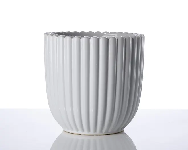 En hvid keramisk beholder med lodrette riller og bølget kant. Overfladen er blank, og formen er cylindrisk med en let afrundet bund. Designet er moderne og minimalistisk, velegnet til både dekoration og praktisk brug.
