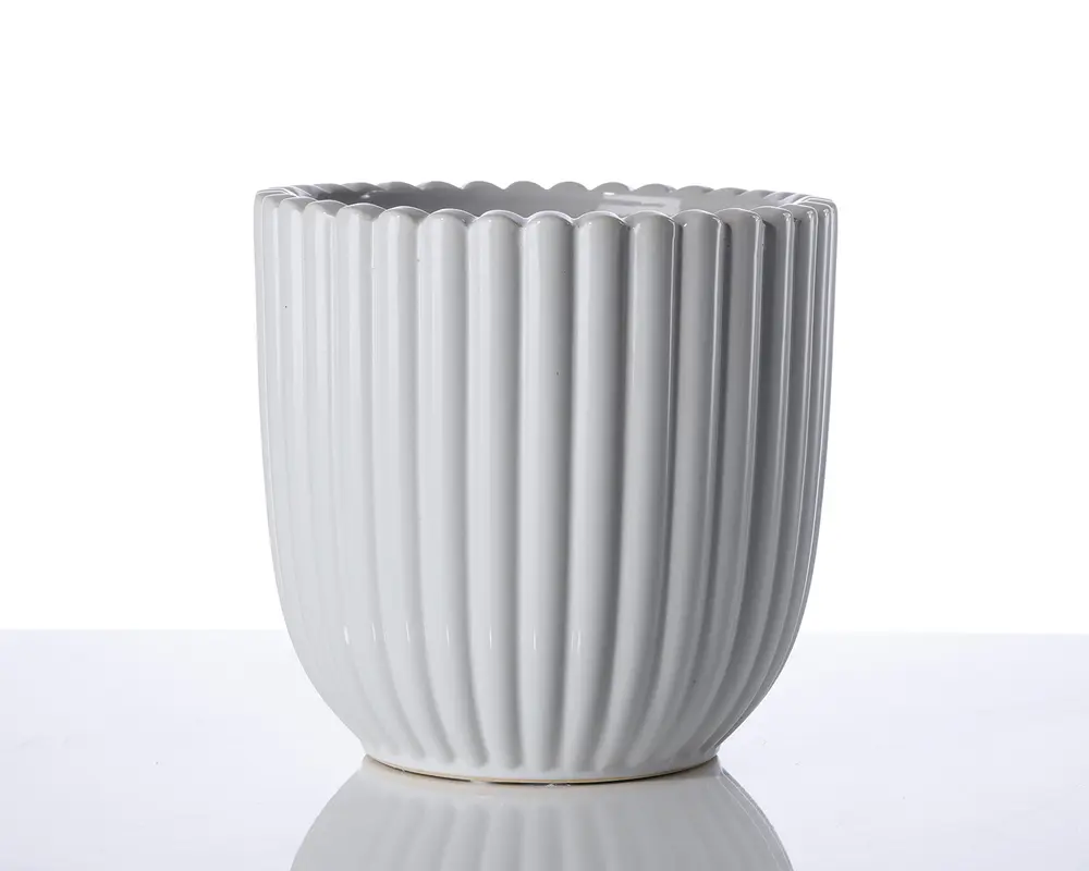 En hvid keramisk beholder med lodrette riller og bølget kant. Overfladen er blank, og formen er cylindrisk med en let afrundet bund. Designet er moderne og minimalistisk, velegnet til både dekoration og praktisk brug.