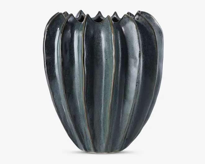 En keramisk vase med en blank mørkeblå og sort overflade, der har et lodret rillet design, som minder om formen på et græskar eller en melon. Den øverste kant er bølget med skiftevis høje og lave punkter, hvilket giver en bølgende effekt. Vasen har et moderne og kunstnerisk udtryk med diskrete farve- og teksturvariationer langs rillerne.