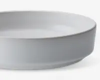 En rund, hvid keramikskål med høje, lige sider og en glat, mat overflade. Skålen har et minimalistisk design uden mønstre eller dekorationer, hvilket gør den velegnet til både hverdags- og festborddækning.