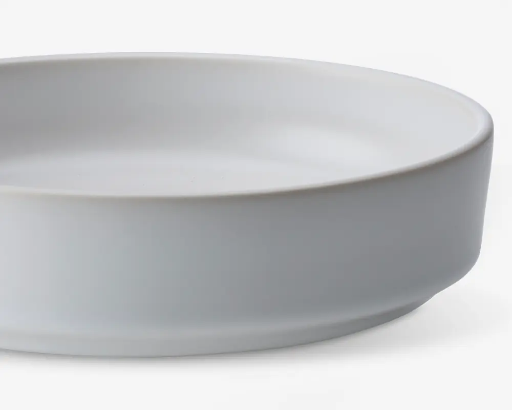 En rund, hvid keramikskål med høje, lige sider og en glat, mat overflade. Skålen har et minimalistisk design uden mønstre eller dekorationer, hvilket gør den velegnet til både hverdags- og festborddækning.