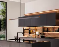 Moderne køkken med matte sorte skabe og et slankt, minimalistisk design. De øverste skabe er uden greb og har en glat, flad overflade. Bagvæggen og de åbne hylder har varme trætoner med integreret LED-belysning, der fremhæver glas, service og dekorative genstande. Køkkenøen har en sort bordplade med integreret vask og en høj, vinklet sort vandhane. En lang, lineær pendellampe hænger over øen og understreger det moderne udtryk. Store vinduer giver naturligt lys og udsigt til grønne omgivelser udenfor.