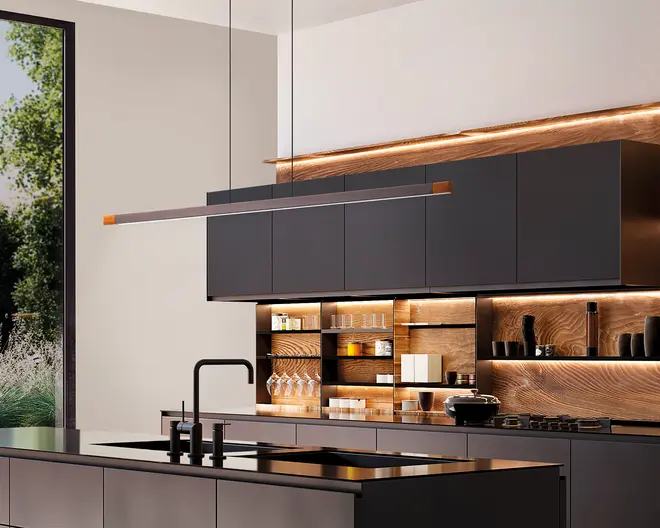 Moderne køkken med matte sorte skabe og et slankt, minimalistisk design. De øverste skabe er uden greb og har en glat, flad overflade. Bagvæggen og de åbne hylder har varme trætoner med integreret LED-belysning, der fremhæver glas, service og dekorative genstande. Køkkenøen har en sort bordplade med integreret vask og en høj, vinklet sort vandhane. En lang, lineær pendellampe hænger over øen og understreger det moderne udtryk. Store vinduer giver naturligt lys og udsigt til grønne omgivelser udenfor.