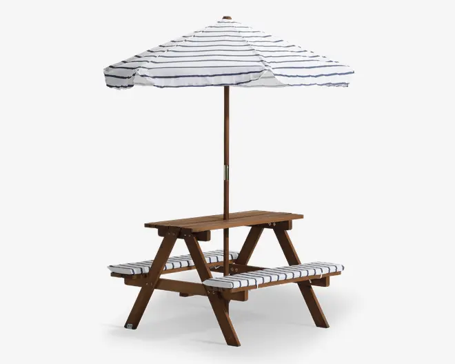 Træ-picnicbord med to fastmonterede bænke og et centralt hul til en stor parasol. Parasollen har en hvid dug med tynde, vandrette, mørkeblå striber. Begge bænke har matchende hvide hynder med mørkeblå striber for ekstra komfort. Bordet og bænkene har en naturlig træfinish og er velegnet til udendørs brug.