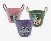 Sæt med tre flettede opbevaringskurve i pastelfarver: lyserød, grøn og lilla. Hver kurv har to solide håndtag og en dekorativ, tredimensionel blomsterapplikation på forsiden med kronblade og en tekstureret midte i matchende farver. Kurvene er lavet af blødt, snoet reb, hvilket giver dem en fleksibel, men struktureret form.