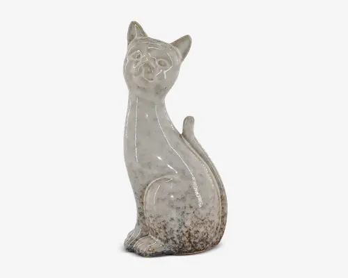 Keramikfigur formet som en siddende kat med lang hals og oprejste ører. Overfladen har en blank, plettet finish i nuancer af offwhite og lysebrun, hvilket giver den et let rustikt og vintage udseende. Ansigtstræk og kropskonturer er diskret markeret, hvilket tilføjer et minimalistisk udtryk til figuren.