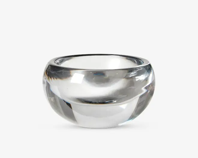 En klar, rund glasskål med tykke vægge og en glat, poleret overflade. Skålen har en bred åbning og en dyb, afrundet bund, hvilket giver den et solidt og elegant udseende. Glassets gennemsigtighed gør det nemt at se indholdet.