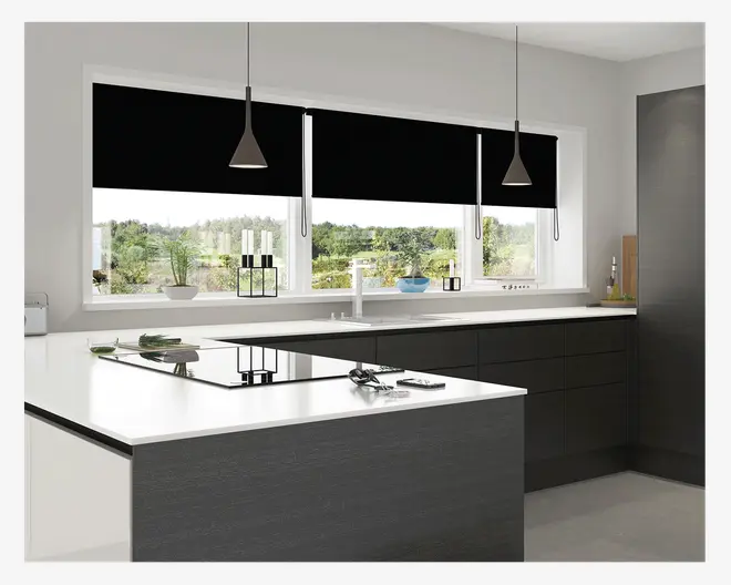 Moderne køkken med glatte, grebsfri mørke skabe og hvide bordplader. Køkkenet har en stor køkkenø med integreret induktionskogeplade og minimalistiske pendellamper hængende over. Vinduerne er dækket af sorte rullegardiner, og vindueskarmen er pyntet med små potteplanter og enkel dekoration. Designet er rent og moderne med et monokromt farveskema.