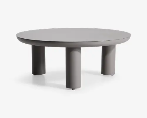 Rundt bord med en glat, mat grå overflade og fire tykke, cylindriske ben. Designet er minimalistisk og moderne med rene linjer og et solid, robust udtryk. Benene er jævnt fordelt og placeret tæt på kanten, hvilket giver stabilitet og et nutidigt look.