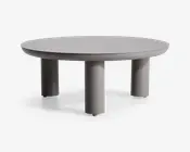 Rundt bord med en glat, mat grå overflade og fire tykke, cylindriske ben. Designet er minimalistisk og moderne med rene linjer og et solid, robust udtryk. Benene er jævnt fordelt og placeret tæt på kanten, hvilket giver stabilitet og et nutidigt look.
