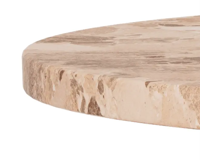 Nærbillede af en tyk, rund bordplade lavet af natursten med et beige og lysebrunt marmoreret mønster. Kanten er let affaset og viser den teksturerede, upolerede stenoverflade, hvilket fremhæver materialets naturlige variationer og rå udseende.