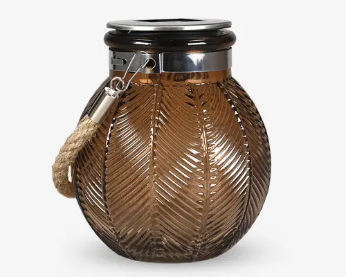 Rund glasbeholder i ravfarvet glas med et tekstureret bladmønster på overfladen. Beholderen har en blank sølvfarvet metalring foroven og et kraftigt, naturligt rebhåndtag, der er fastgjort med en metalclips, hvilket giver et rustikt og elegant udtryk.
