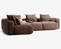 En moderne, modulopbygget sofa med dybt sæde og brede armlæn, betrukket med et tekstureret brunt stof. Sofaen har bløde, fyldige ryg- og sædehynder for ekstra komfort og leveres med flere matchende pyntepuder. Der ligger et lyst tæppe og et magasin afslappet på sædet, hvilket giver et hyggeligt og indbydende udtryk.