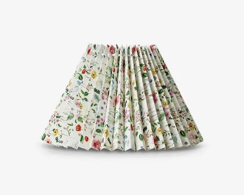 En plisseret nederdel med hvid baggrund og et farverigt blomsterprint. Blomsterne er i forskellige nuancer af rød, gul, pink, blå og grøn, hvilket giver et livligt og iøjnefaldende mønster. Nederdelen har en struktureret, fyldig form på grund af de skarpe plisseringer, og stoffet ser let og luftigt ud.