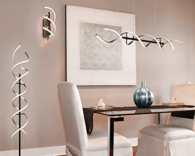 Moderne belysningsarmaturer med et karakteristisk spiraldesign. Gulvlampen og væglampen har begge LED-lysbånd snoet i en helixform, monteret på slanke sorte stativer. Loftlampen over bordet har også et bølget, spiralformet LED-bånd ophængt i tynde wirer, hvilket giver et skulpturelt udtryk. Armaturerne udsender et blødt, varmt hvidt lys og tilfører rummet et moderne og kunstnerisk præg.