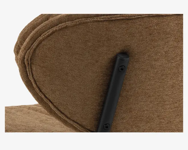 Nærbillede af en brun stofoverflade med synlige syninger og en sort metalstøtte fastgjort med to skruer. Stoffet har en tekstureret finish, og syningerne følger den buede kant, hvilket indikerer et polstret og komfortabelt design.