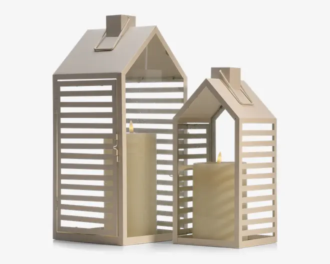 Sæt med to dekorative lanterner i husformet design, fremstillet af lyst beige metal med lameller. Hver lanterne har et saddeltag og en rektangulær bund samt en hængslet dør for nem adgang. Indeni hver lanterne står et stort bloklys, som giver en varm og hyggelig stemning. De åbne lameller i siderne lader lyset skinne igennem og skaber et mønstret skær.